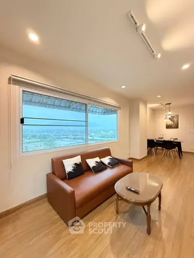 Modern living room with large window and stylish dining area, featuring wooden flooring and elegant lighting.