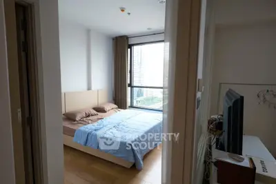 Cozy bedroom with large window offering city view, featuring wooden flooring and modern furnishings.