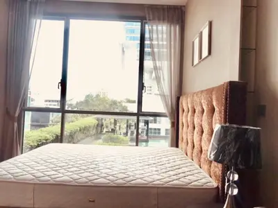Spacious bedroom with large window offering a stunning view, featuring a plush headboard and elegant lamp.