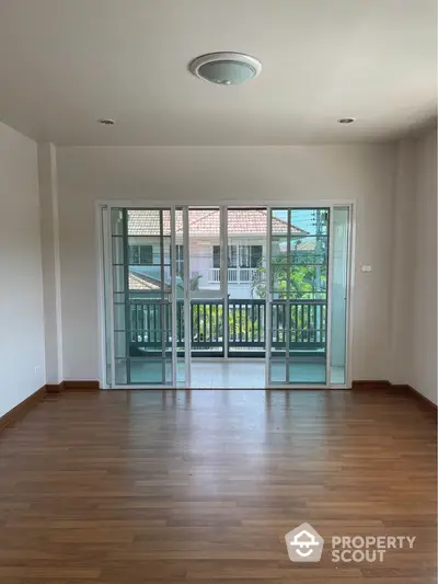 Spacious and well-lit living room with polished hardwood floors and large glass doors leading to a charming balcony, perfect for modern living.