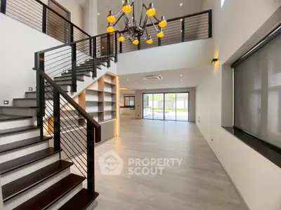 Spacious modern living room with elegant staircase and large windows for natural light.