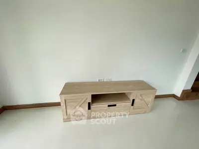 Minimalist wooden TV stand in a bright, unfurnished room with white walls and floor.