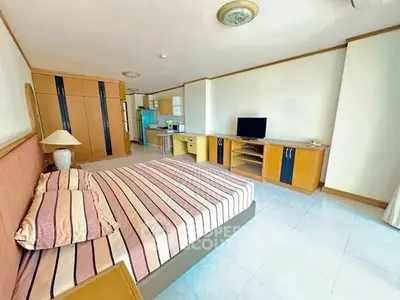 Spacious bedroom with modern furnishings and open kitchen layout in a bright apartment.