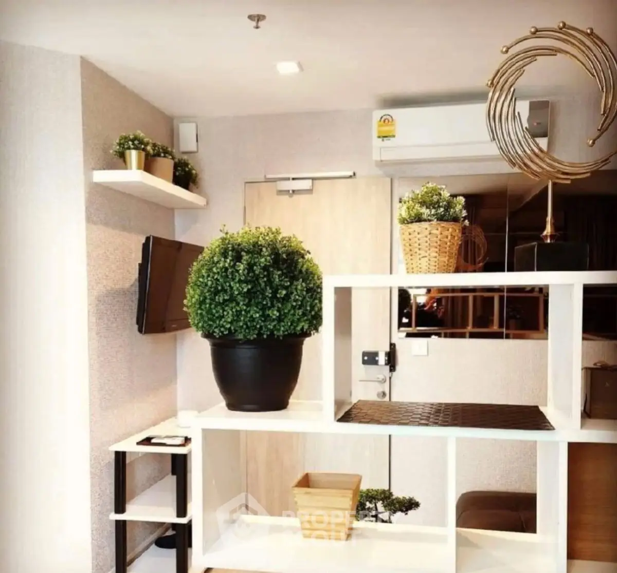 Modern living room with stylish decor and indoor plants, featuring a mounted TV and air conditioning unit.