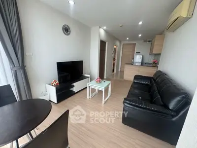 Modern living room with sleek black leather sofa and flat-screen TV, open to a compact kitchen area.