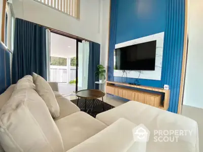 Modern living room with stylish blue accent wall and large TV, featuring cozy beige sofa and open patio view.