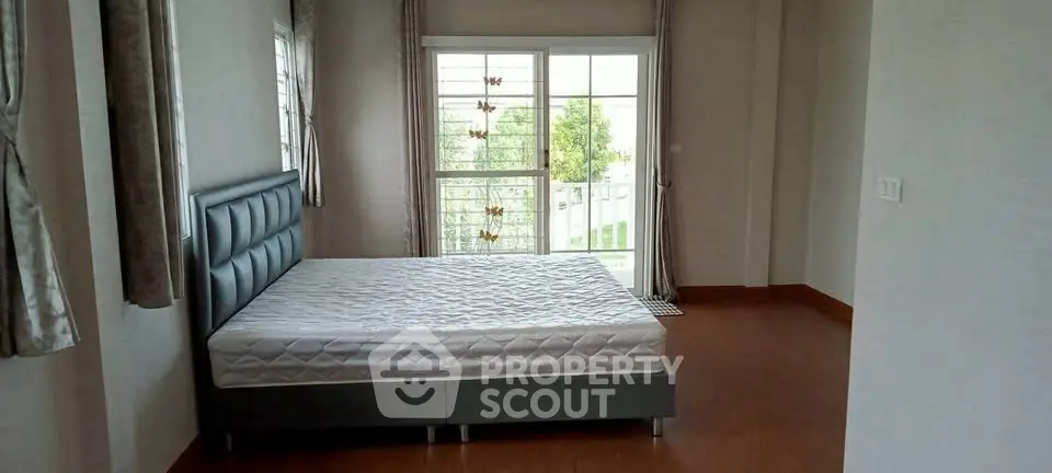 Spacious bedroom with large window and natural light, featuring a modern bed and hardwood floors.