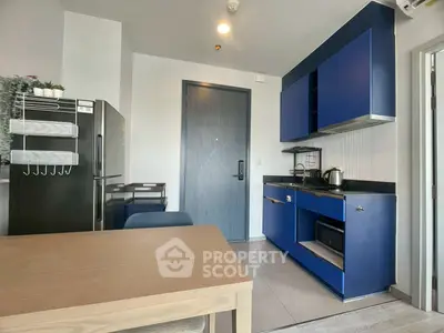 Modern kitchen with blue cabinets and sleek appliances in a compact apartment setting.