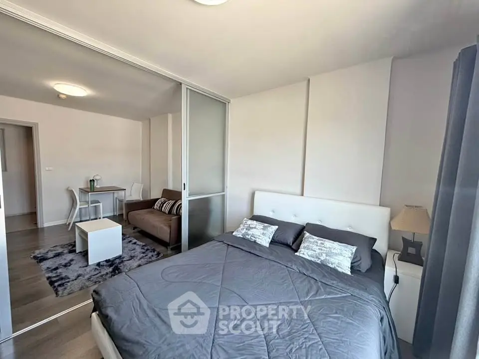 Modern bedroom with sliding doors and cozy living area in open-plan apartment.