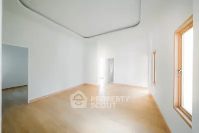 Spacious empty room with wooden flooring and large windows.