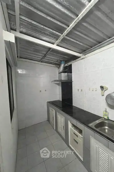 Compact kitchen with tiled walls and metal roof, featuring a sink and countertop.