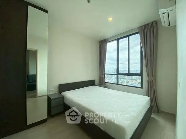 Modern bedroom with large window offering city view, featuring a comfortable bed and sleek wardrobe.