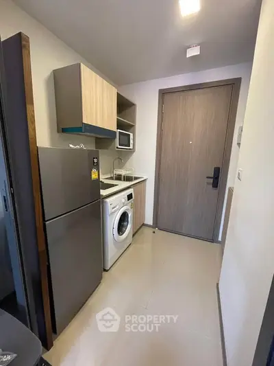 Modern compact kitchen with washing machine and fridge in stylish apartment.