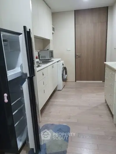 Modern kitchen with open fridge and washing machine, sleek cabinetry and wooden flooring.