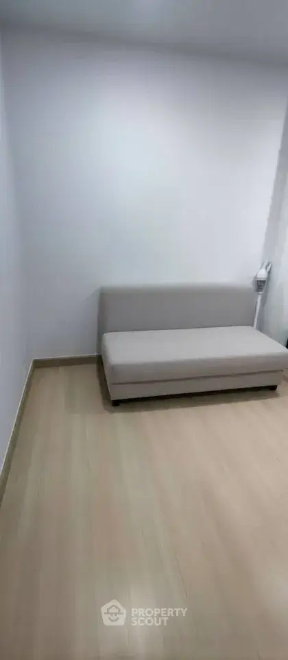 Minimalist small living room with a compact sofa and light wood flooring.