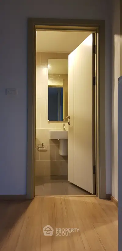 Modern bathroom with open door, sleek fixtures, and neutral tiles in a cozy apartment setting.