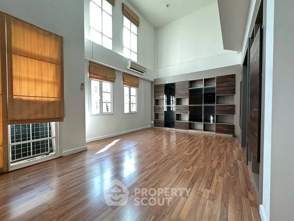 Spacious living room with high ceilings and large windows, featuring elegant wooden flooring and built-in shelving.