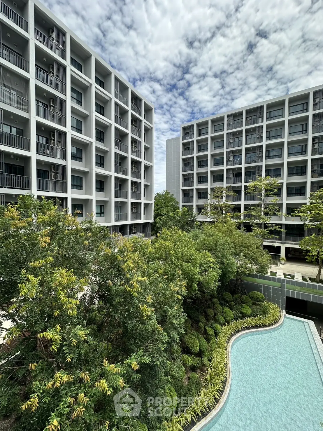 Modern apartment buildings with lush garden and pool view under a cloudy sky.
