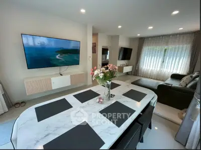 Modern living room with elegant decor and large TV, featuring a stylish dining table and cozy seating area.