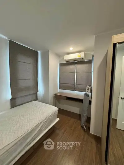 Cozy bedroom with wooden flooring, single bed, and built-in desk under window with blinds.