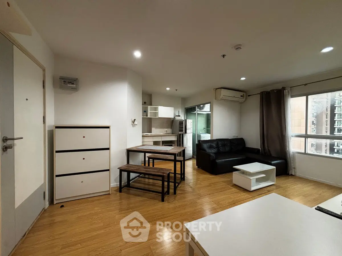 Modern open-plan living room with kitchen and dining area, featuring wooden flooring and natural light.