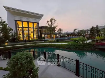 Luxurious modern building with large windows overlooking a serene pond at sunset.