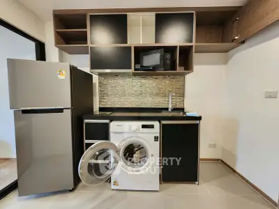 Modern kitchen with washing machine, fridge, and microwave in sleek apartment.