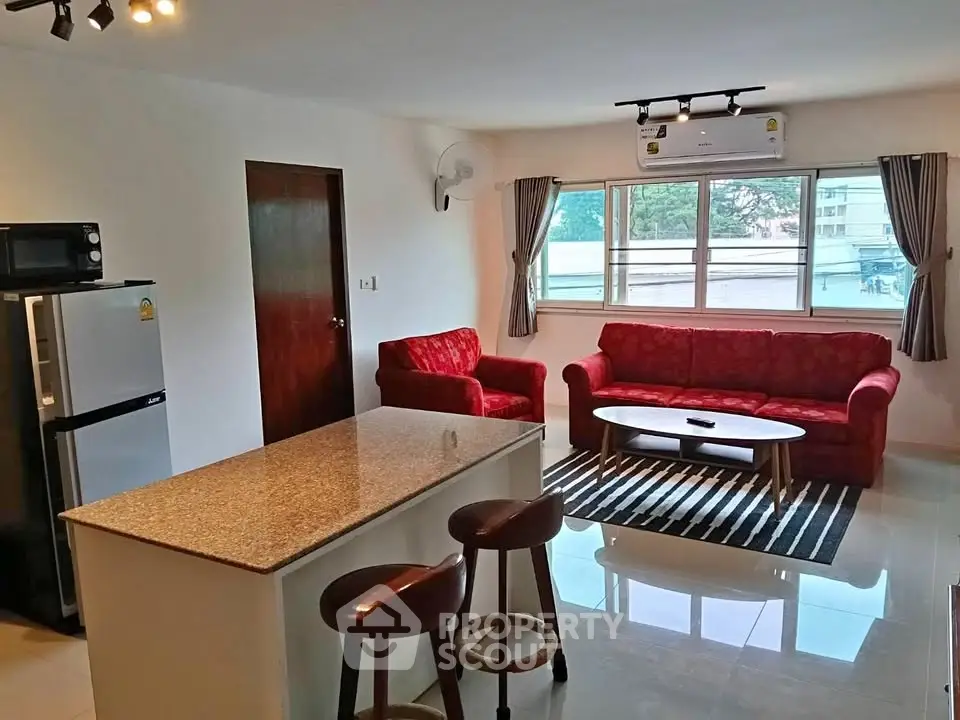 Spacious living room with modern kitchen and stylish red sofas in a bright apartment.