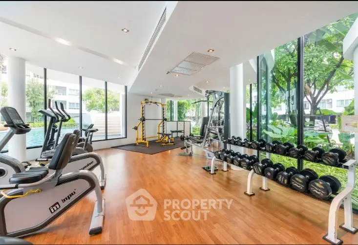 Spacious gym with modern equipment and large windows overlooking lush greenery.