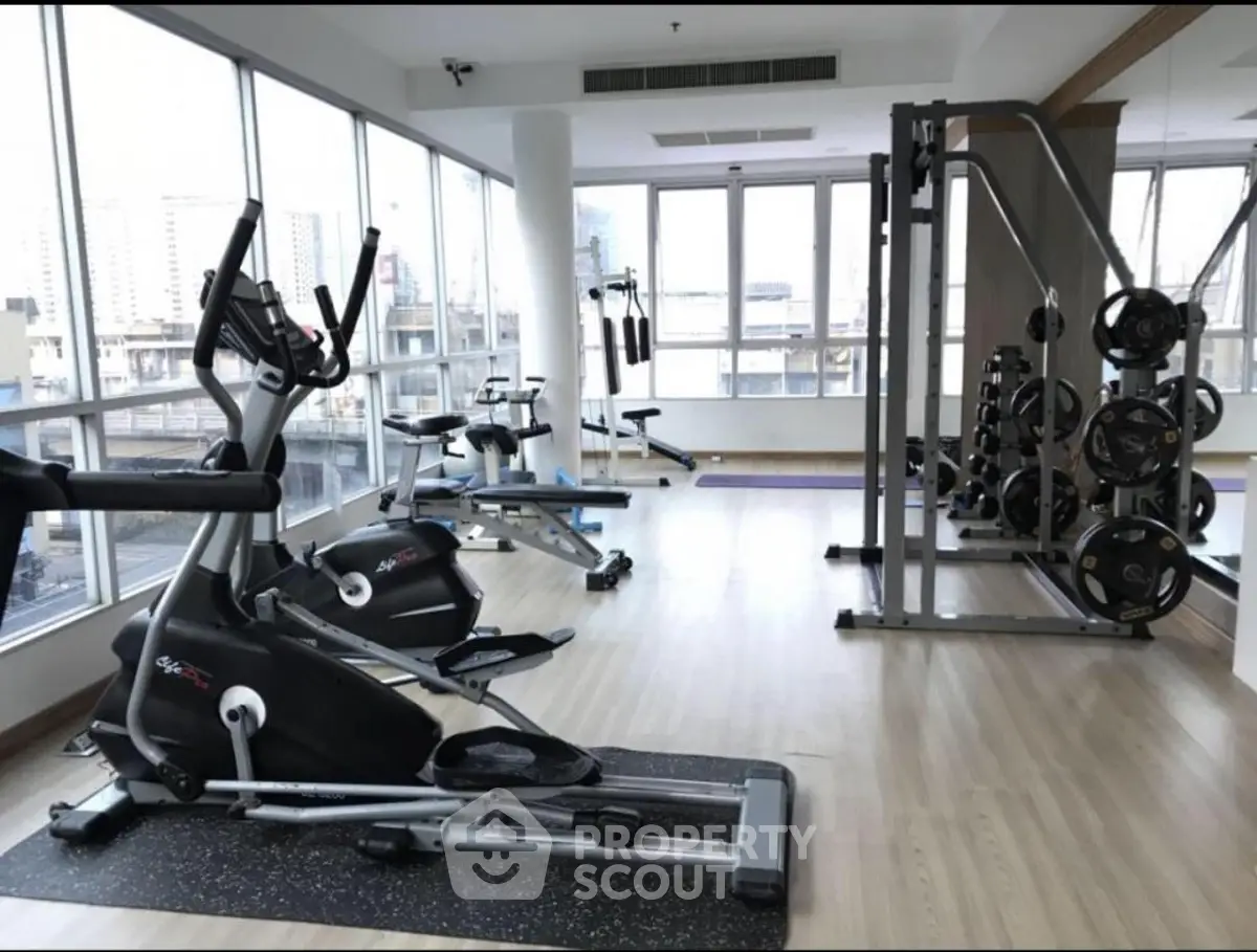 Spacious gym with modern equipment and city view in luxury apartment building.