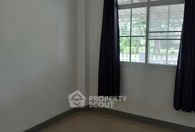 Minimalist empty room with large window and dark curtains, offering natural light and garden view.