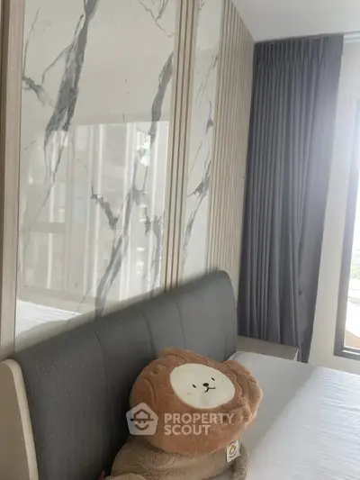 Modern bedroom with stylish marble accent wall and plush bear pillow on bed
