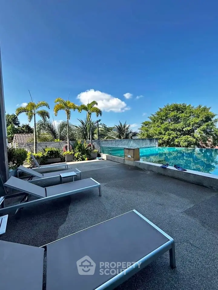 Luxurious outdoor pool area with sun loungers and tropical landscaping under a clear blue sky.