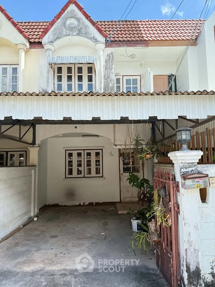 Charming townhouse with red-tiled roof and gated entrance, featuring a cozy front porch and classic architectural details.