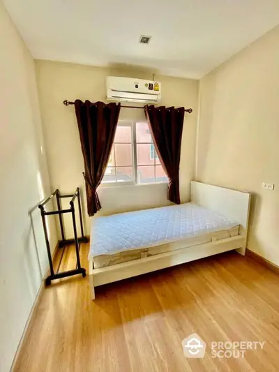 Cozy bedroom with natural light, wooden flooring, air conditioning unit, and minimalist decor, perfect for modern living.