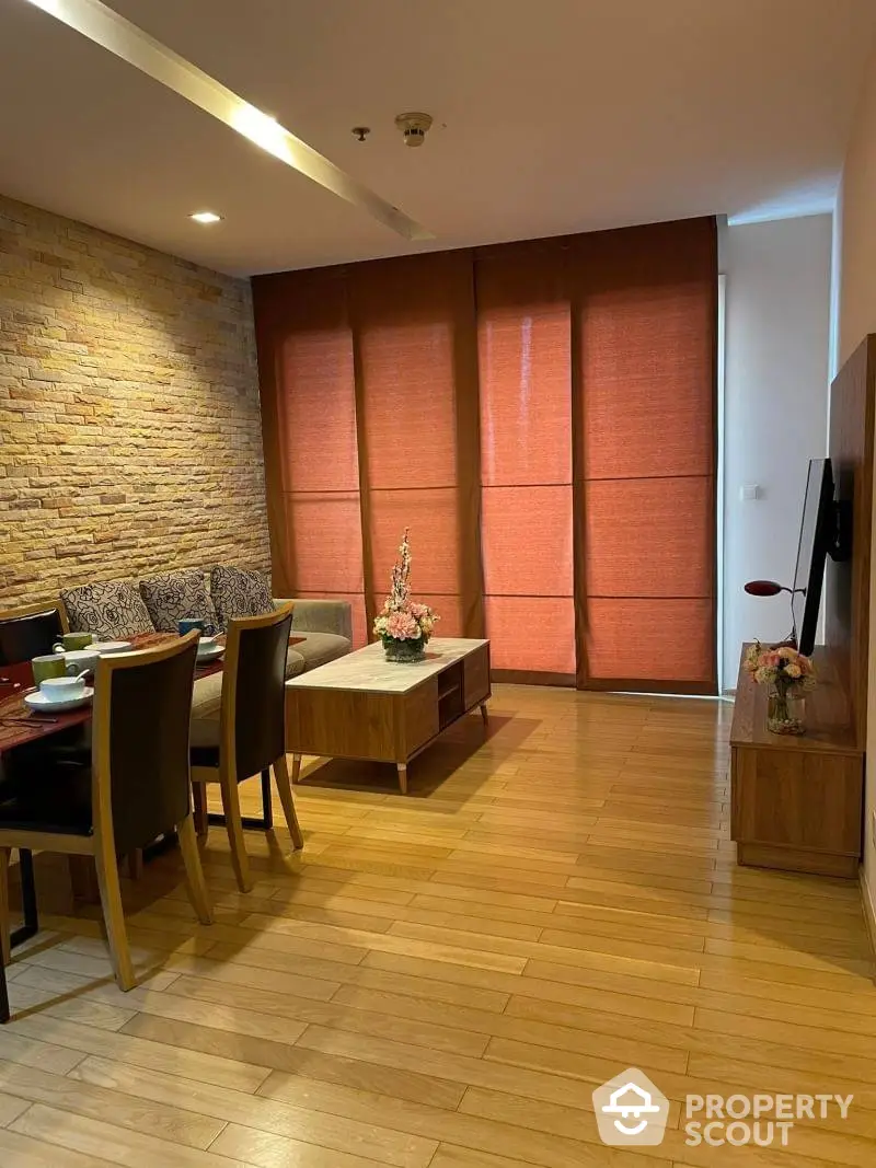 Warm and inviting living space with rich wooden floors, a cozy dining area, and an accent brick wall complemented by stylish red drapes, creating a perfect blend of modern and rustic charm.