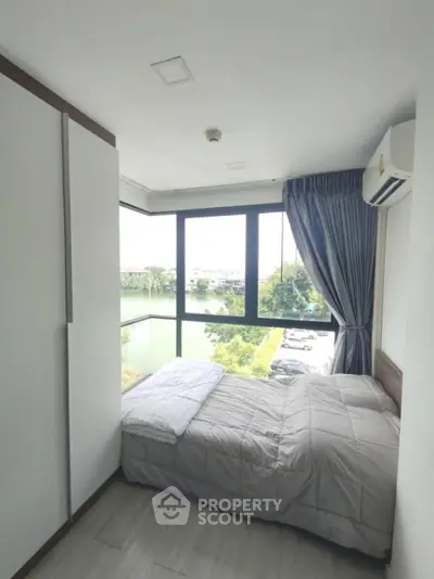 Modern bedroom with large windows offering stunning river view in high-rise apartment.
