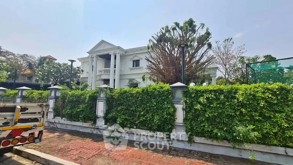 Luxurious white mansion with classical architecture and lush greenery in a prestigious neighborhood.