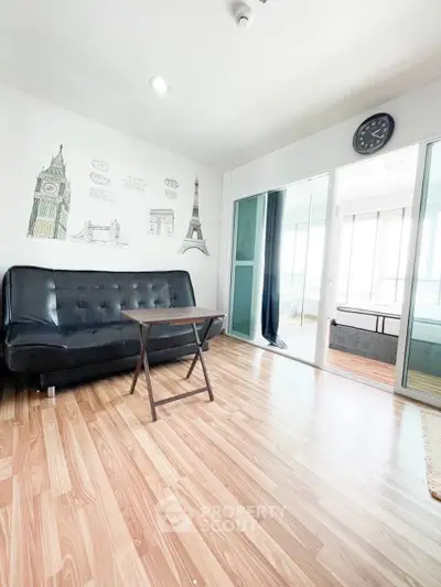 Modern living room with stylish decor and wooden flooring, featuring a black sofa and wall art.