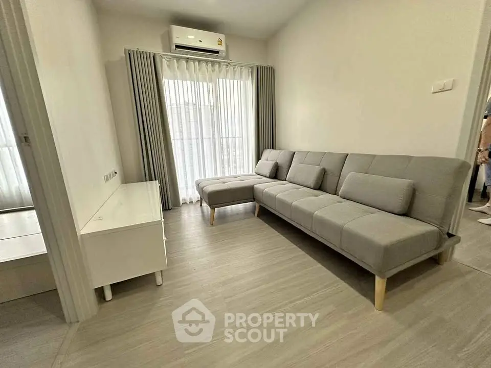 Modern living room with sleek gray sofa and natural light from large window, perfect for relaxation.