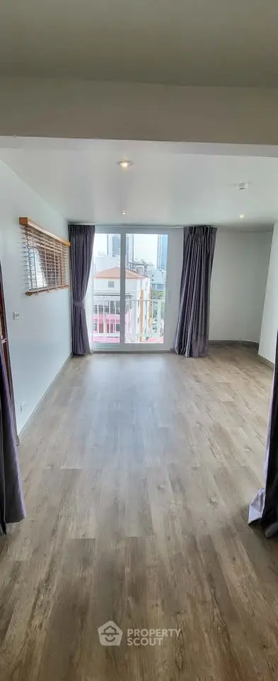 Spacious room with large window and city view, featuring elegant wooden flooring and modern curtains.