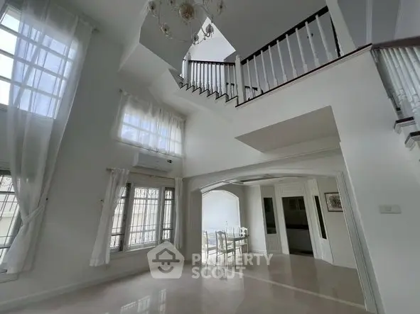 Spacious two-story living room with elegant staircase and dining area, featuring large windows and high ceilings.