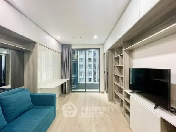 Modern living room with blue sofa and TV, featuring built-in shelves and balcony view.