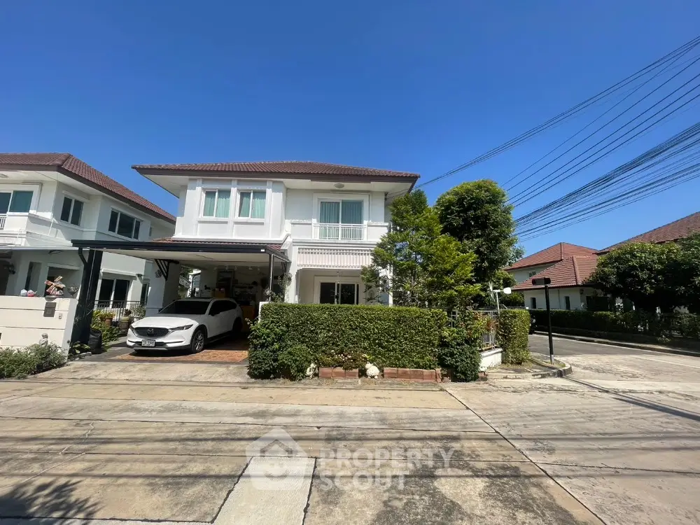 Charming two-story house with carport in a serene neighborhood, featuring lush greenery and modern architecture.