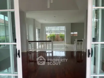 Spacious open-plan living area with hardwood floors and large windows offering garden views.