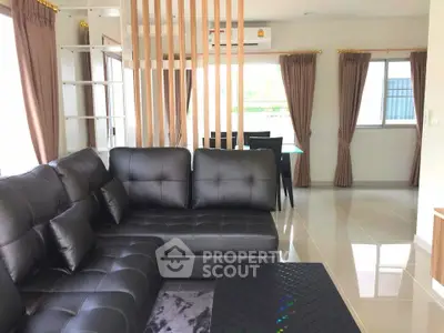 Modern living room with sleek black leather sofa and dining area, featuring elegant decor and ample natural light.