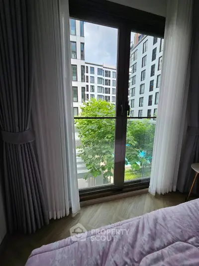 Modern bedroom with large window offering a view of contemporary apartment buildings.