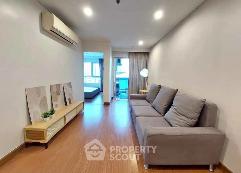 Modern living room with cozy gray sofa and wooden flooring, leading to a bright bedroom with balcony view.