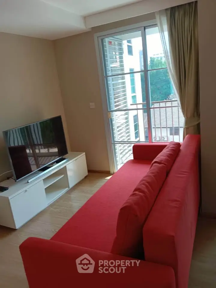 Modern living room with red sofa and large TV, featuring a bright window view.