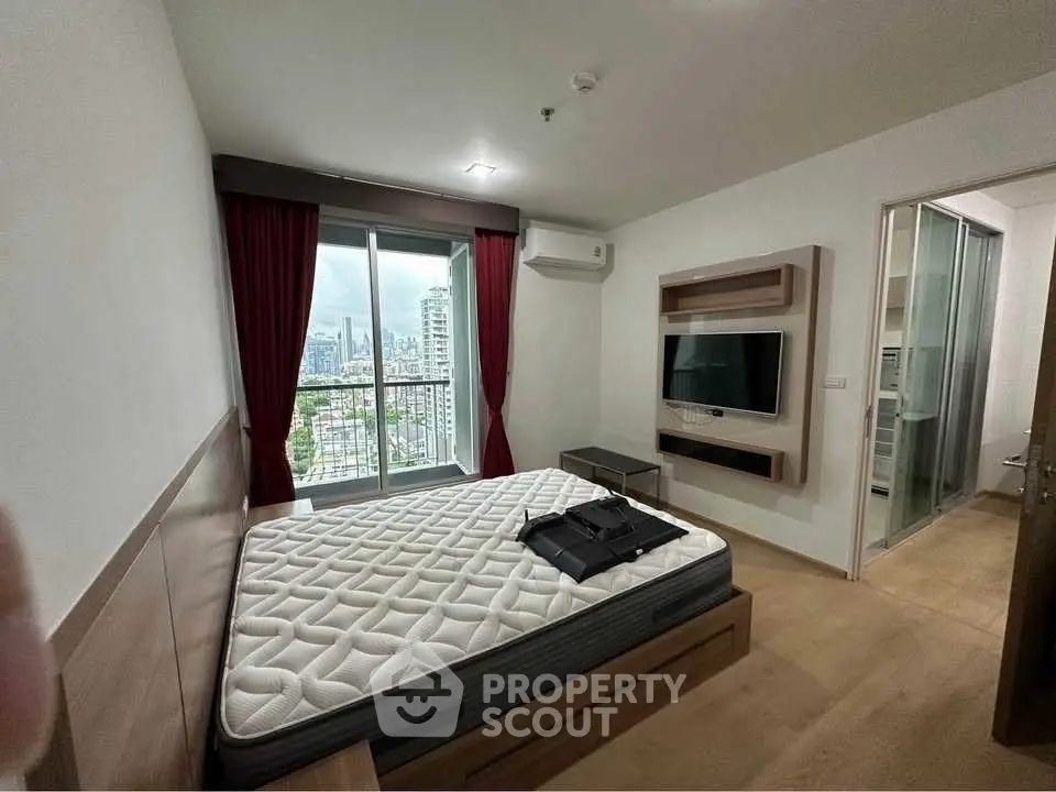 Modern bedroom with city view, featuring a wall-mounted TV and large window with red curtains.